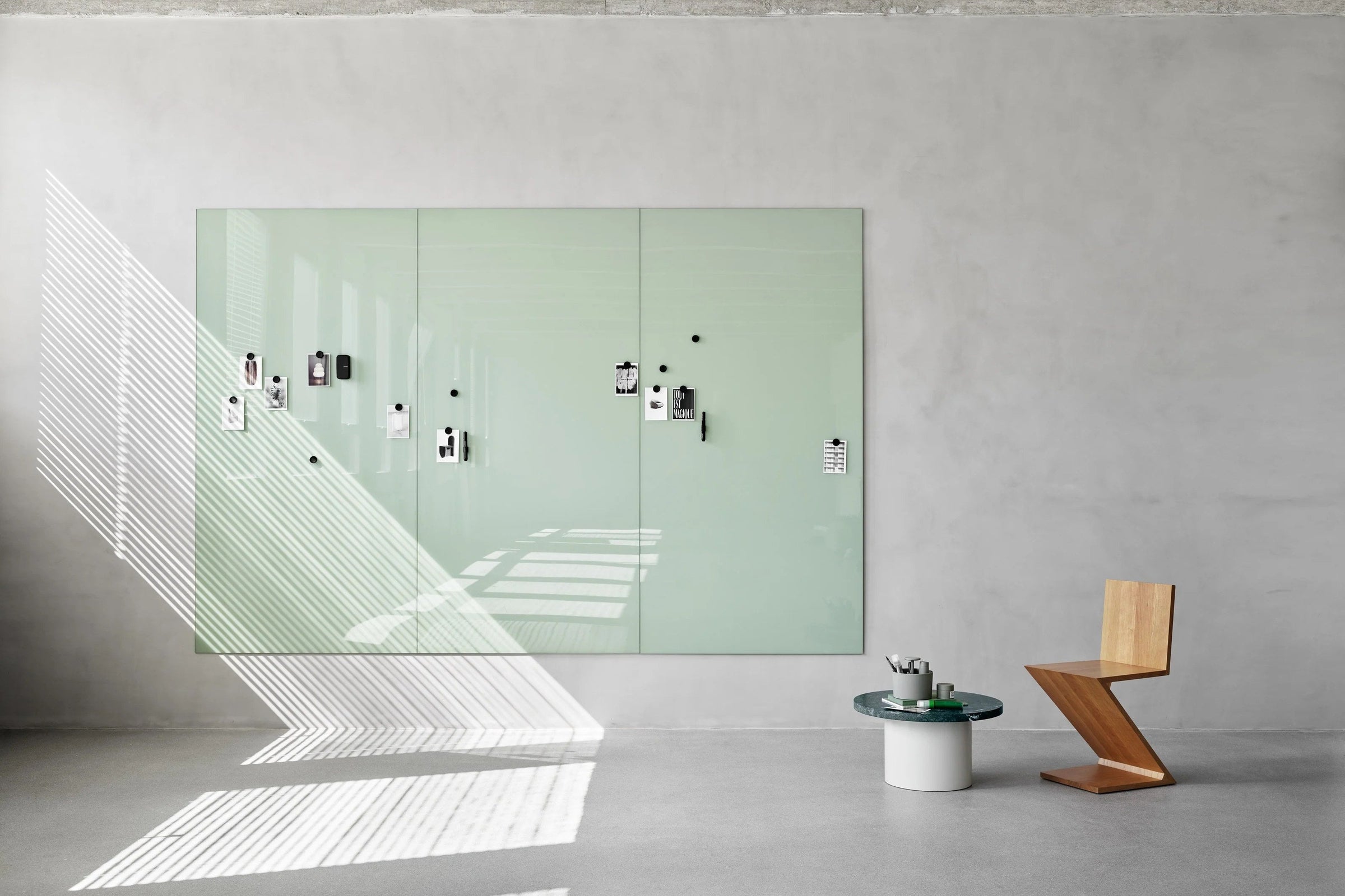 Continuous coloured glass writing wall spanning a meeting room behind a timber table and task chairs