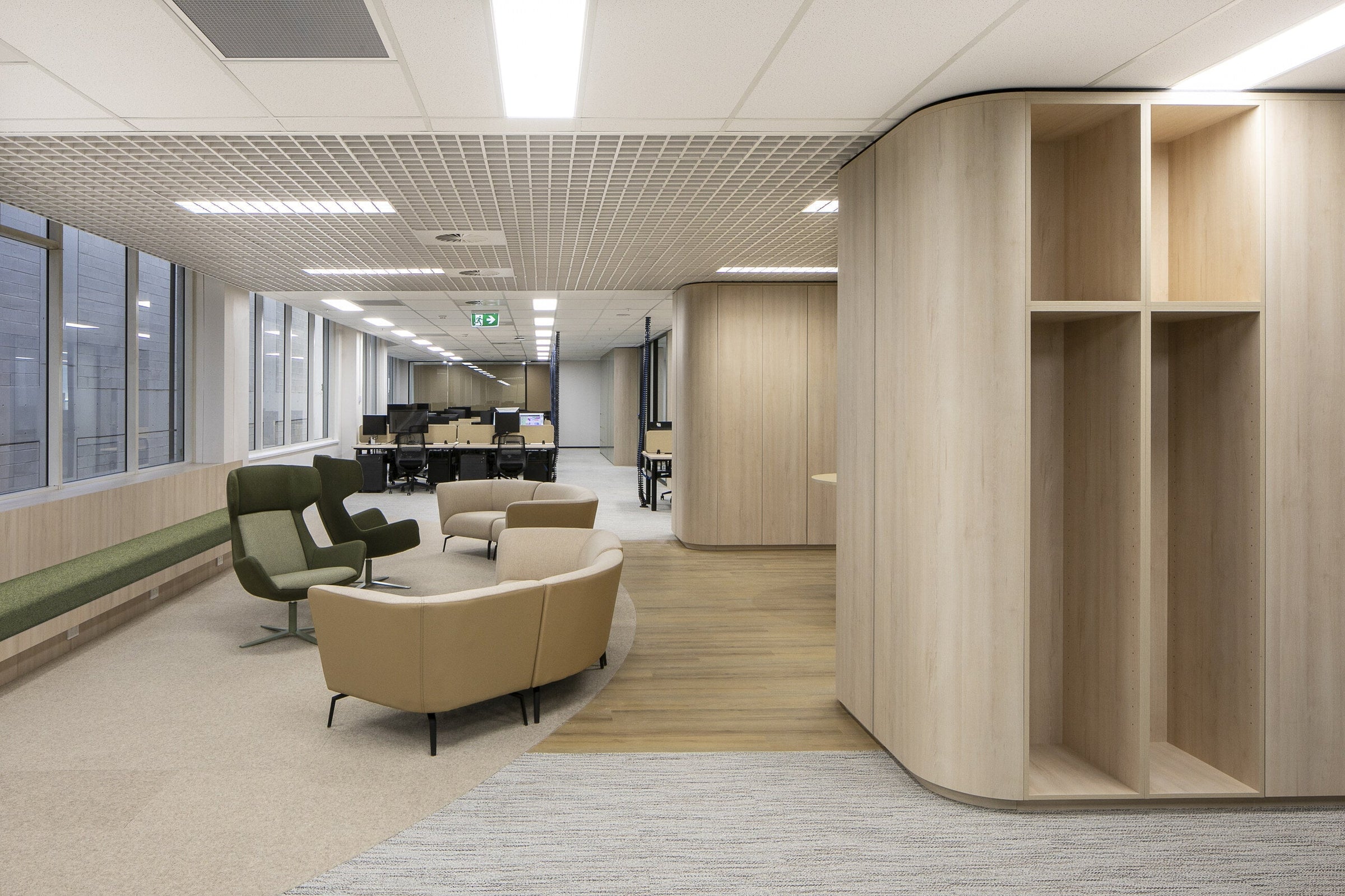 Open timber shelving joinery running along an office wall, with lounge seating and a low table on the floor in front of it
