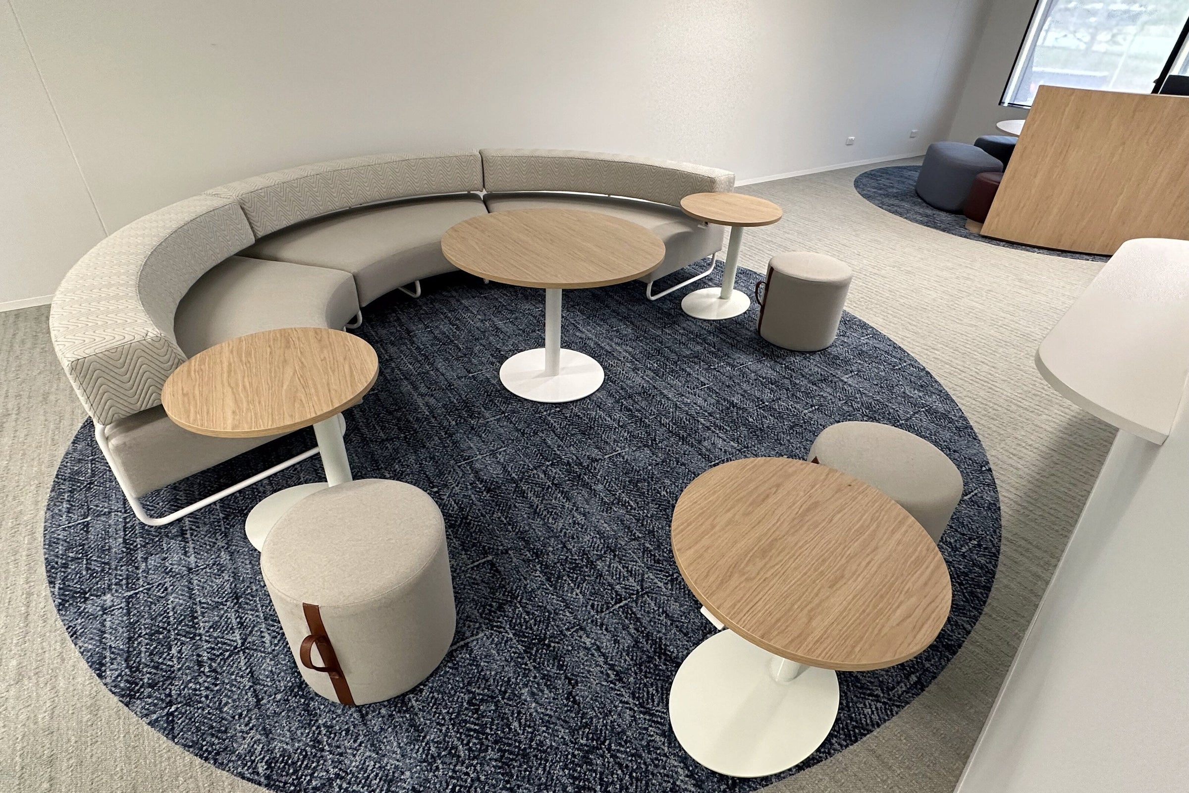 Round collaboration hub on the WentWest floor in Western Sydney, with a curved upholstered banquette, round timber tables and drum ottomans on a round carpet inset